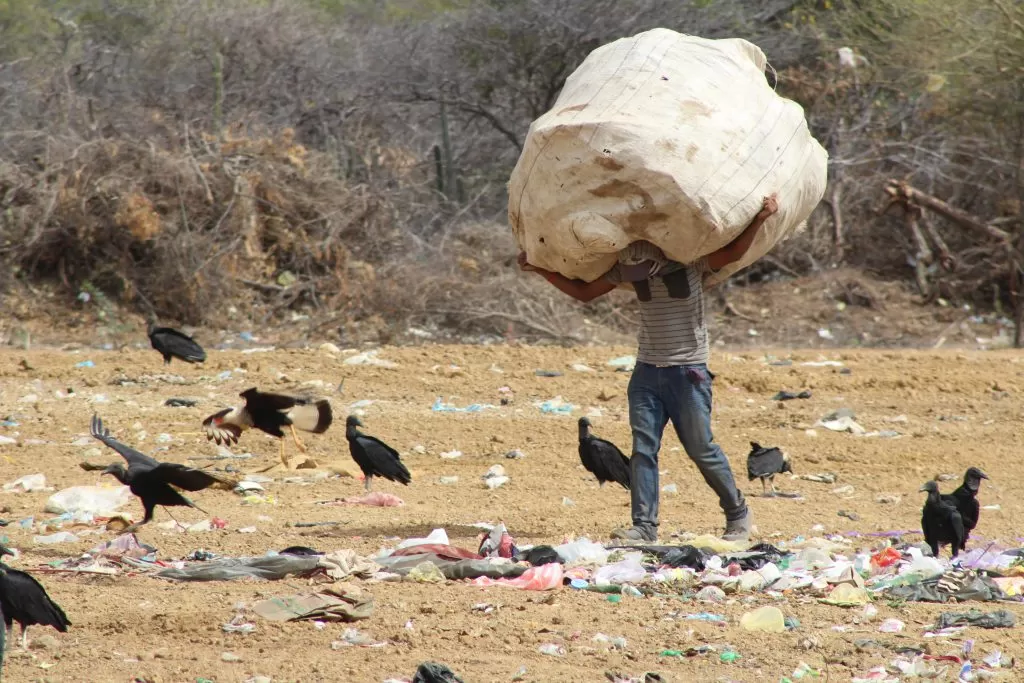 Wayuu man carrying a huge bag on his shoulders in a landfill.